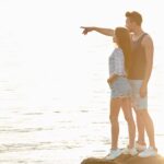 Romantic young couple standing on the rock and looking at horizon together